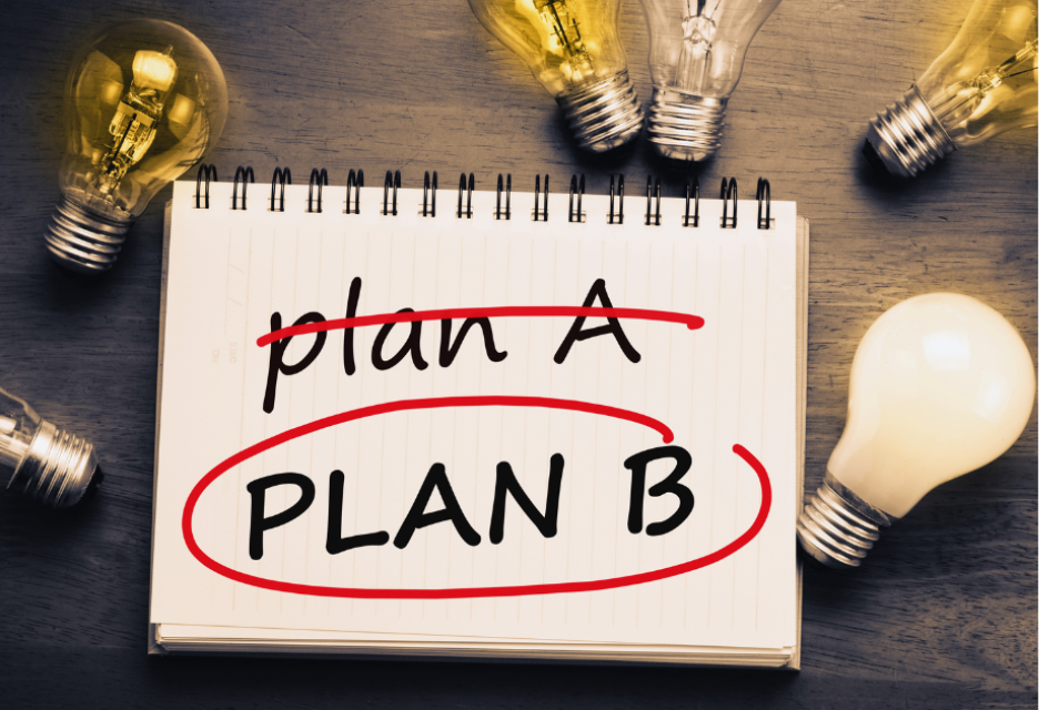 Notebook showing “Plan A” crossed out and “Plan B” circled, surrounded by light bulbs on a wooden desk.